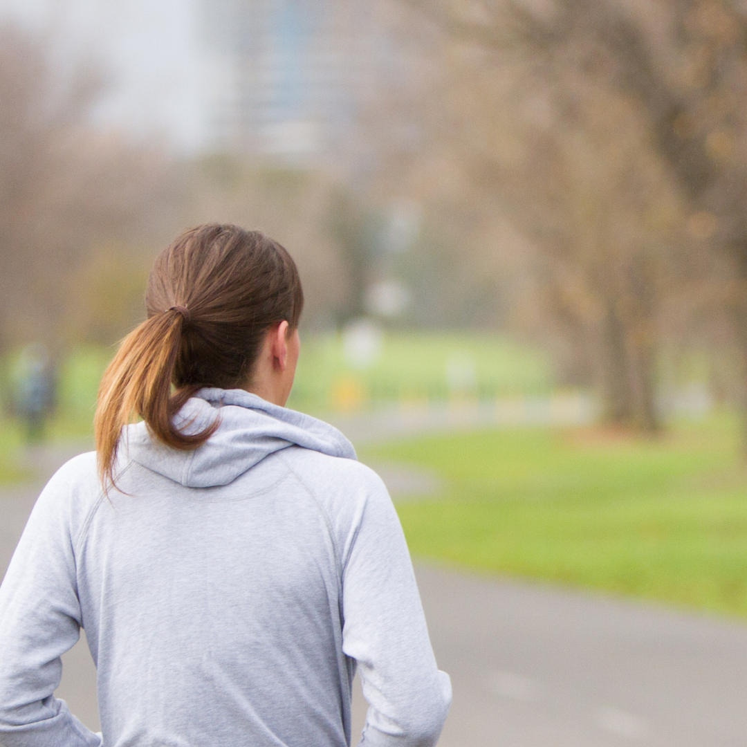 woman with a pony tail, waring a grey hoodie walking in the park